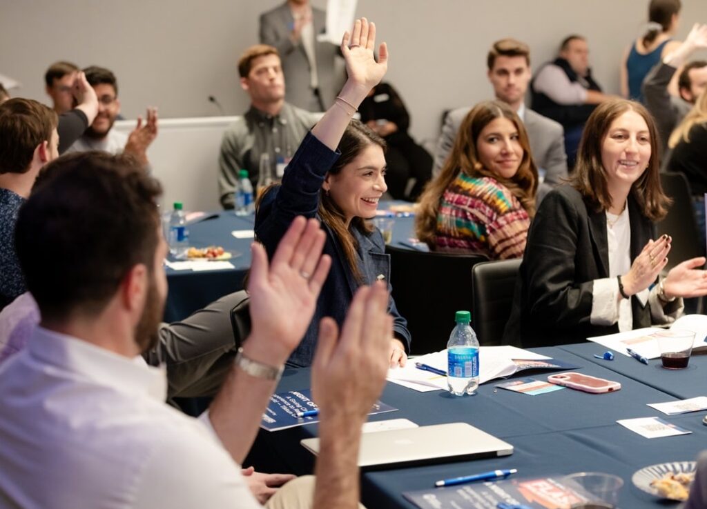 People sitting at tables, including a woman raising her hand.