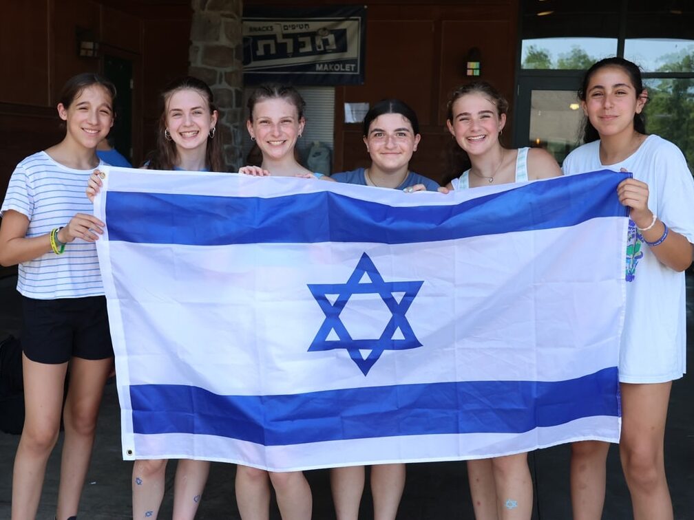 A group of girls smiling and holding an Israeli flag at summer camp