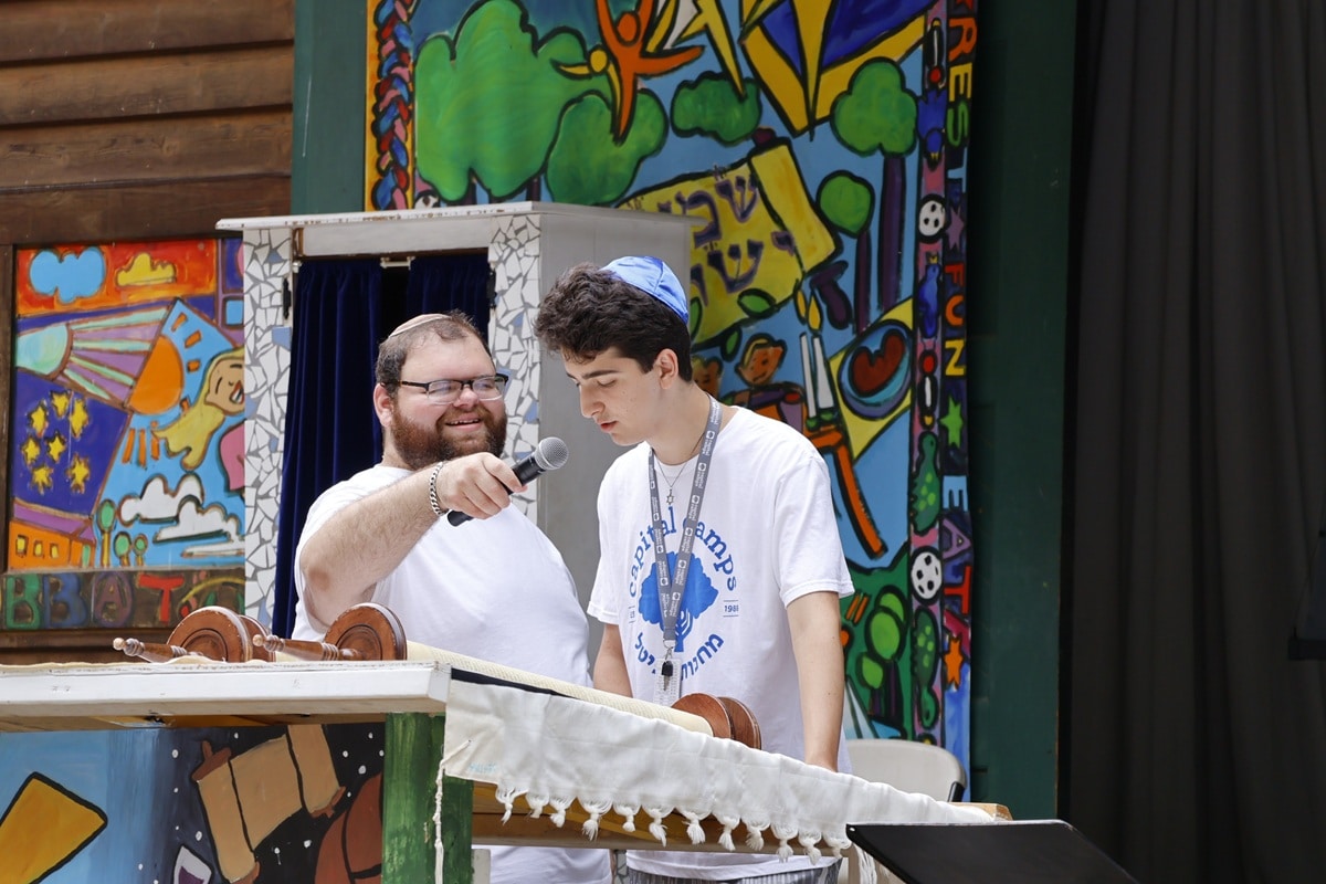 A man holding a microphone for a teen reading the Torah