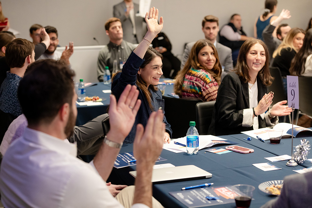 Woman raises hand at a table full of people clapping for her.