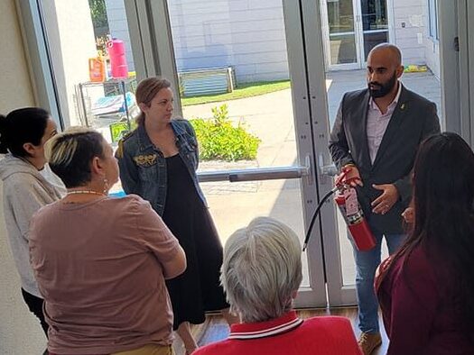 A man holding a fire extinguisher speaks to a small group by a door