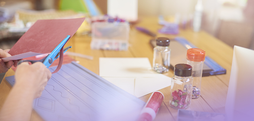 A person is sat at a table cutting paper whilst doing an arts and crafts hobbies