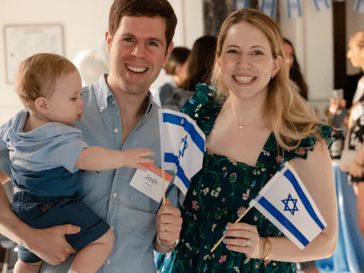 A smiling couple holding their baby and Israeli flags