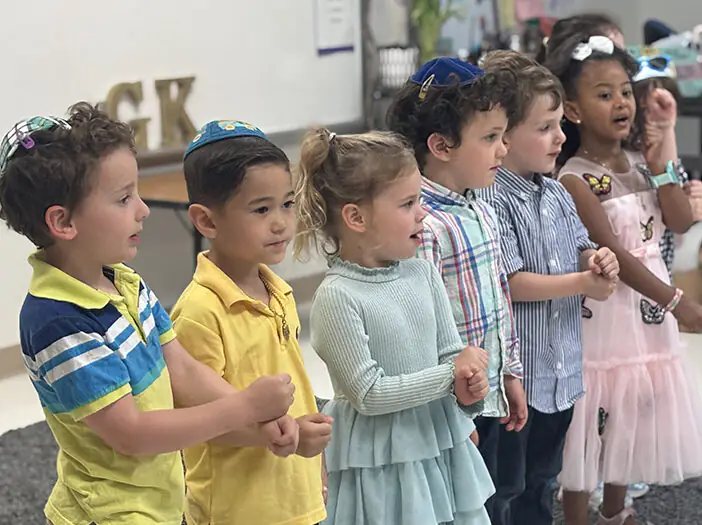 Preschool age children stand in a line singing a song.